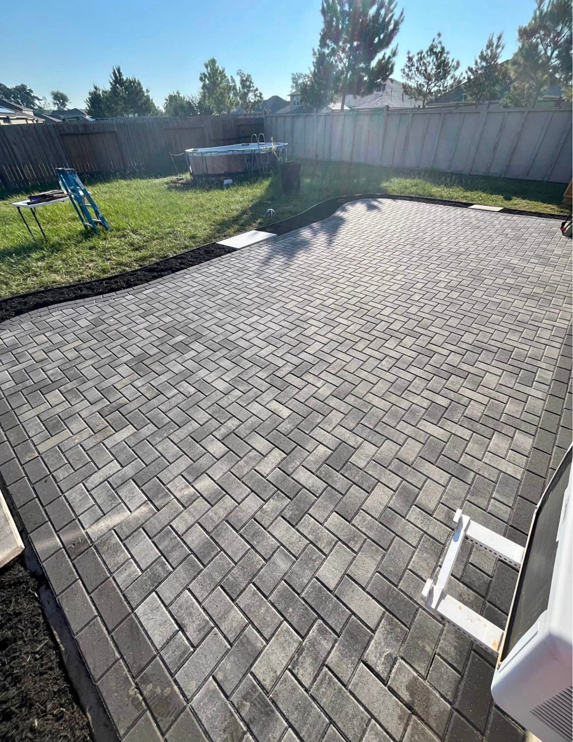 Newly laid grey interlocking paver patio in a herringbone pattern before sand sealing