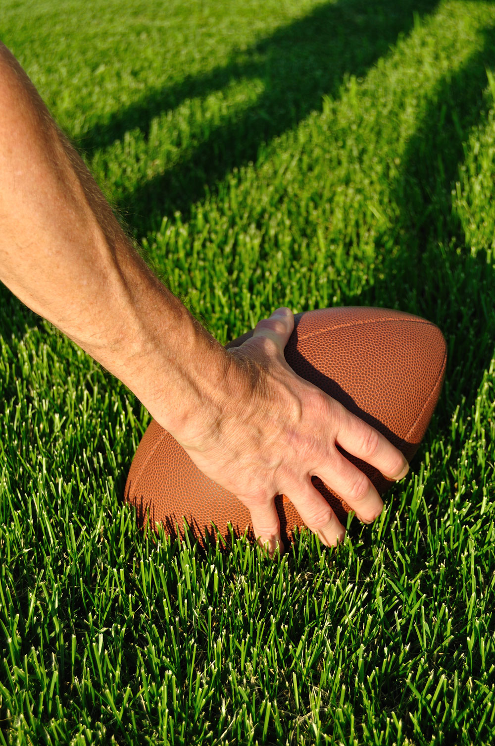 Hand picking up a football on turf